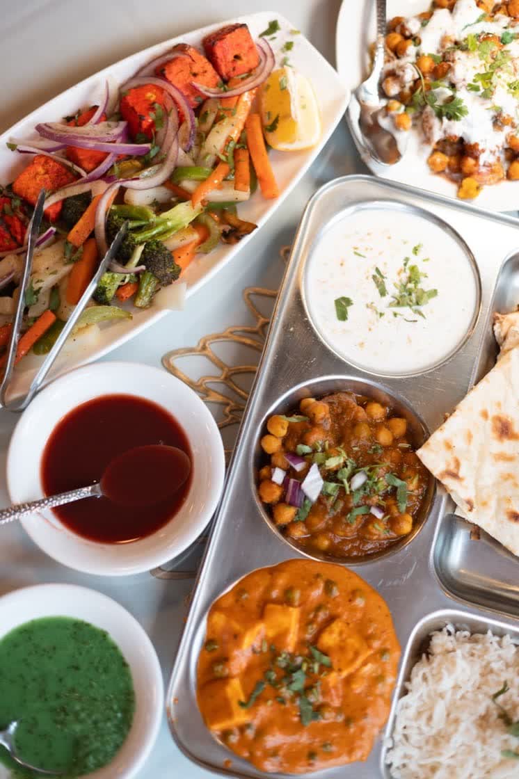 Paneer curry, chickpea curry, raita, rice and naan on a serving tray